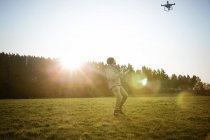 Hombre de pie en el prado y el avión no tripulado volador - foto de stock