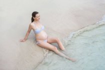 Mujer embarazada sentada en la playa de arena - foto de stock