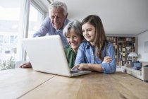 Grand-parents et leur petite-fille avec ordinateur portable à la maison — Photo de stock