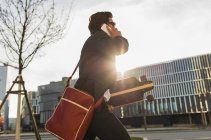 Young businessman walking the city with skateboard, using mobile phone — Stock Photo
