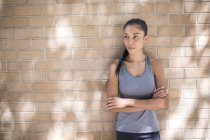 Retrato de atleta femenina confiada apoyada contra la pared de ladrillo - foto de stock