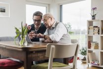 Homme âgé avec petit-fils assis à table dans le salon avec ordinateur portable et smartphone — Photo de stock