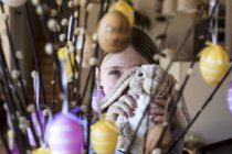 Chica escondida detrás de conejito de Pascua y ramitas de sauces de coño decoradas con huevos de Pascua - foto de stock