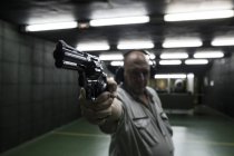 Человек со слуховыми защитниками, нацеленный с револьвером на стрельбище в помещении — стоковое фото