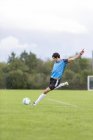 Jogador de futebol chutando bola no campo de esportes — Fotografia de Stock