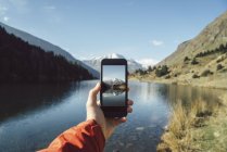 Francia, Pirineos, Carlit, mano masculina tomando una foto en el lago de montaña - foto de stock