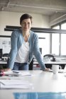 Portrait of confident businesswoman leaning on desk in office — Stock Photo