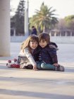 Garotinho e menina sorridentes sentados lado a lado no chão da cidade — Fotografia de Stock