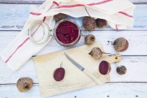 Whole and halved beetroots and preserving jar of pickled beetroots on white wood — Stock Photo