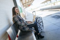 Businesswoman sitting on a bench at train station using a laptop — Stock Photo
