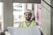 Портрет усміхненого будівельника з планом будівництва на будівельному майданчику — стокове фото