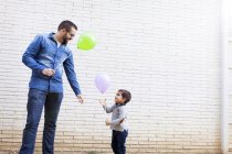 Отец и его маленький сын с воздушными шарами перед белой кирпичной стеной — стоковое фото