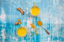 Two glasses of curcuma milk with ingredients on blue shabby surface — Stock Photo