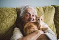 Seniorin sitzt auf Couch und umarmt Kätzchen — Stockfoto