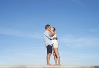 Casal sênior abraçando e beijando em uma parede na frente do céu — Fotografia de Stock