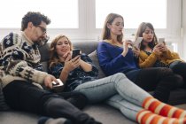 Чотирьох друзів з смартфонами на канапі у вітальні, проведення часу — стокове фото