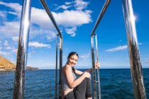 Retrato de uma jovem mulher sorridente sentada em uma plataforma em frente ao mar — Fotografia de Stock