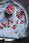 Bowl of dried rose blossoms and a silver spoon on cloth and tray — Stock Photo