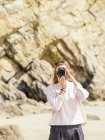 Mujer de pie en la playa, tomando una foto con cámara - foto de stock