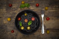 Schüssel Spaghetti al nero di seppia mit Tomaten und Basilikumblättern auf dunklem Holz — Stockfoto
