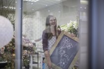 Happy florist carrying a board in flower shop — Stock Photo