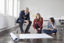 Businessman and two women in office looking at construction plan — Stock Photo
