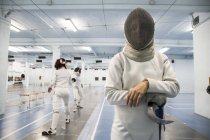 Scherma femminile indossando maschera di recinzione con partita di scherma in background — Foto stock