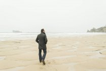 Homme marchant sur la plage avec les mains dans les piquets — Photo de stock