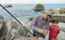 Grandfather teaching grandson fishing at the sea — Stock Photo
