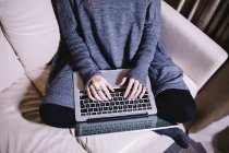 Jeune femme assise sur le canapé en utilisant un ordinateur portable, vue partielle — Photo de stock