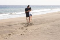 Счастливая влюбленная пара, гуляющая по пляжу — стоковое фото