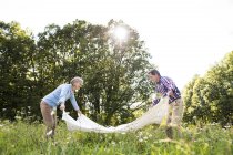 Senior couple spreading out blanket on a meadow — Stock Photo