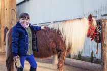 Portrait of smiling girl grooming pony looking at camera and smiling — Stock Photo