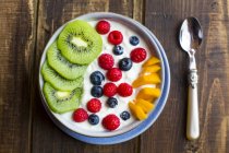 Bowl with yogurt and blueberries, kiwi, mango and raspberries, spoon on wood — Stock Photo