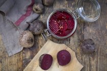 Preserving jar of pickled beetroots and whole and halved beetroots on dark wood — Stock Photo