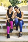 Две спортивные девушки сидят на лестнице и смотрят на мобильный телефон. — стоковое фото