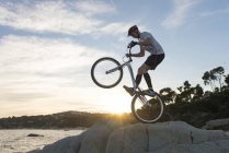 Велосипедист, стрибки на скелі на пляж Льорет де Мар на заході сонця — стокове фото