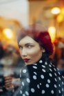 Retrato de jovem mulher usando chapéu vermelho olhando pela janela de um pub à noite — Fotografia de Stock