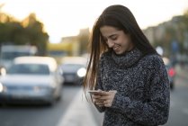 Улыбающаяся молодая женщина с мобильного телефона на улице — стоковое фото