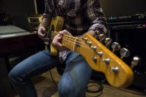Man playing an electric guitar in the control room of a recording studio — Stock Photo