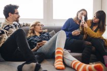 Quatro amigos com smartphones no sofá na sala de estar — Fotografia de Stock