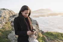 Испания, Ферроль, портрет улыбающейся женщины с помощью смартфона на берегу — стоковое фото