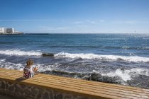 Mulher sentada em um banco na frente do mar e usando smartphone, Tenerife, Espanha — Fotografia de Stock