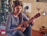 Mulher tocando ukulele na frente da árvore de Natal — Fotografia de Stock