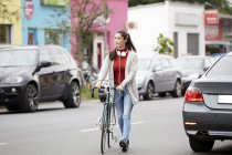 Woman with headphones and bicycle crossing street — Stock Photo