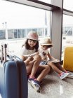 Dos niñas esperando en el aeropuerto, jugando con la tableta digital - foto de stock