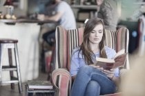 Молодая женщина, сидящая в кафе, читает книгу — стоковое фото