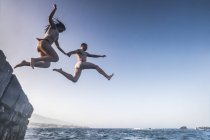 Giovane coppia che salta in mare da roccia — Foto stock