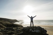 Homme debout sur le rocher à la côte avec les bras tendus — Photo de stock