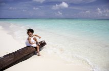 Maldives, fille assise sur une bûche sur une plage — Photo de stock